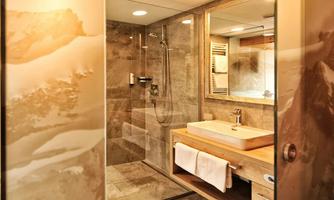 A modern bathroom with a shower and an elegant sink. The walls are clad in gray tiles, and there are wooden details.