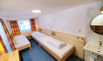 A simple room with two beds and a washbasin. The window offers a view outside, and it is brightly decorated.