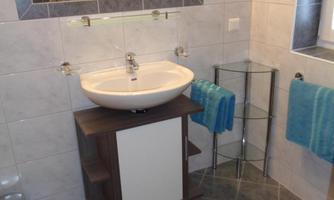 A modern bathroom with a sink on a wooden base and a mirror. The walls are tiled and there are blue towels as well as a rug on the floor.
