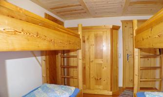 A simple room with two wooden bunk beds. The room has a pleasant wooden ceiling and a wardrobe.
