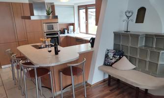 A modern kitchen with wooden shelves, bar stools, and a dining area. It is bright and welcoming designed.