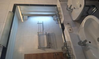 A modern bathroom with two sinks and a large mirror. The space is bright and well-organized, with white tiles and a shower in the background.
