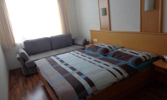 A cozy bedroom with a large bed and a gray sofa. It has bright walls and plenty of natural light.