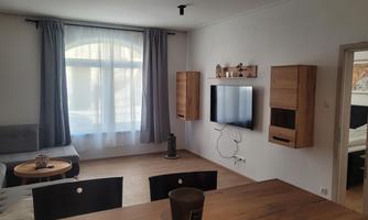A modern living room with a cozy sofa and a television on the wall. Bright curtains let in plenty of daylight.