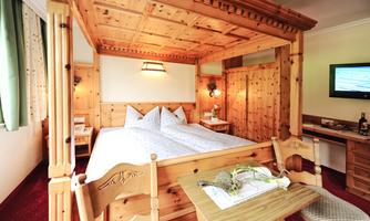 A cozy room with a wooden four-poster bed and warm colors. There is a television and a small table with chairs.