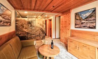 A cozy living space with wooden paneling and modern pictures on the walls. In the foreground is a round table with a bottle of wine and glasses.