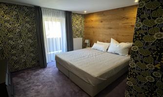 A modern bedroom with a large bed and a cozy atmosphere. The walls are decorated with a floral pattern and there is plenty of natural light.