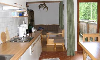 A cozy kitchen with a wood countertop and modern appliances. In the background, there is an area with a couch and a balcony.