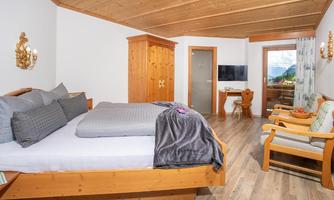 A cozy room with a large bed and wooden décor. There is a desk, a TV, and a beautiful view through the window.