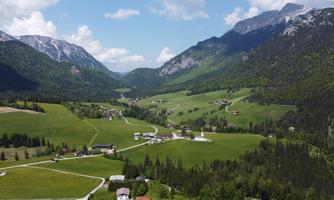 A picturesque landscape with gentle hills and green meadows, surrounded by majestic mountains. The sky is clear and blue, perfect for a view of nature.