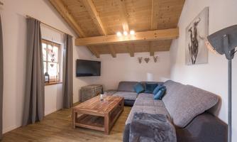 A cozy living room with a wooden ceiling and a large sofa. A wooden table and a television complete the modern ambiance.