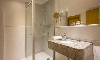 A modern bathroom with a glass shower and a marble sink. The space is bright and well-lit.