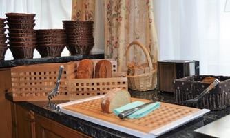 A modern kitchen scene with a wooden cutting board and fresh bread. In the background, stacked baskets and a toaster are visible.
