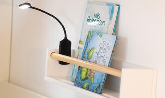 A bookshelf with two children's books and a practical reading lamp. The lamp shines on the books and provides a pleasant atmosphere for reading.