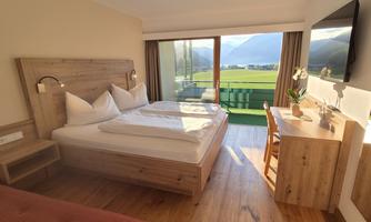 A modern room with a double bed and a desk. Large windows offer a view of nature and plenty of daylight.