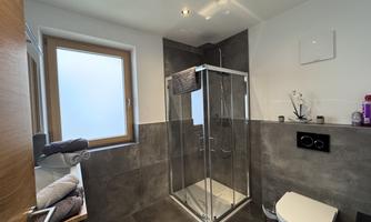 A modern bathroom with a glass shower and a toilet. There are fresh towels and a bright window front.