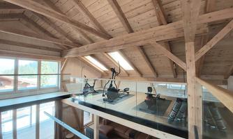 A modern gym in the attic with wooden beams and large windows. There are visible workout machines that offer a view of the surroundings.