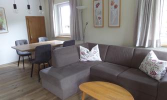 A modern living room with a gray sofa and a wooden table. The walls are bright and adorned with decorative pictures.