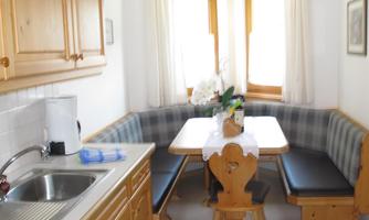 A cozy kitchen with wooden furniture and a seating area. A table stands in the middle, decorated with flowers.