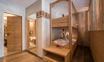 A modern room with a wooden loft bed. There is a mirror, a door, and decorative flowers on a table.