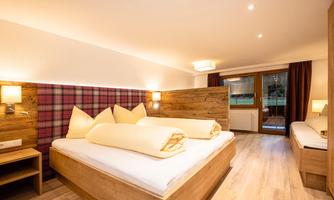 A modern bedroom with wooden decor and cozy beds. The room features a balcony with an outdoor view.
