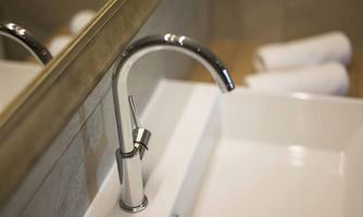 A modern sink with a shiny faucet. In the background are some folded towels.