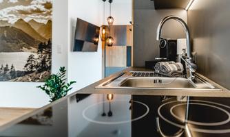 A modern kitchenette with a stylish faucet and cooktops. In the background, decorative elements and a mountain landscape on the wall are visible.