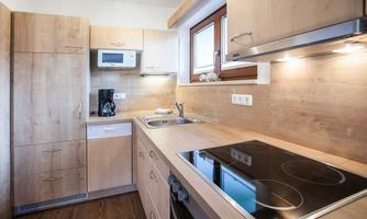 A modern kitchen with wooden surfaces and good amenities. It features a stove, a sink, and a window that lets in plenty of light.