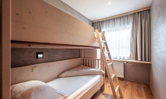 A modern bedroom with a wooden bunk bed. The room has large windows and a warm wooden floor.