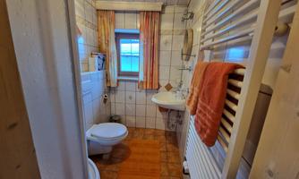 A small bathroom with a toilet, a sink, and a heater. It has bright tiles and an orange bath mat.
