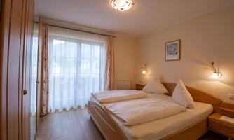 A cozy bedroom with two beds and wooden panels. Large windows let in plenty of light.