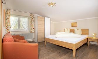 A bright bedroom with a double bed and a cozy red armchair. Large windows provide plenty of daylight and a friendly atmosphere.