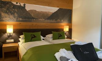 A cozy hotel room with a double bed and green bedding. On the walls are light sources and a beautiful landscape picture.