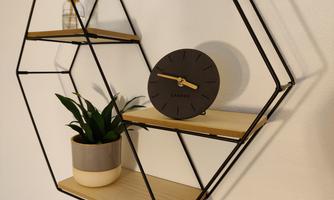 A modern wall shelf in a geometric shape with wooden shelves. It contains a plant, a clock, and a glass container.