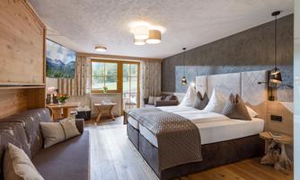 A modern hotel room with a large double bed and a cozy seating area. Large windows let in plenty of natural light and offer a view of nature.