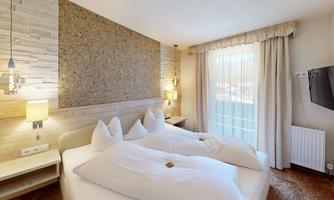 A cozy bedroom with two beds and modern wooden decor. A window with curtains lets in daylight and creates a bright atmosphere.