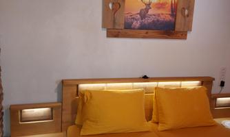 A cozy bedroom with a double bed and yellow pillows. On the wall hangs a picture of a deer in front of an autumn landscape.