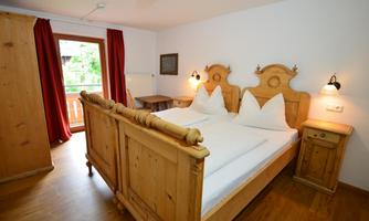 A cozy bedroom with two wooden bed frames and white duvet covers. Curtains in red and a window with a view outdoors give the room an inviting atmosphere.