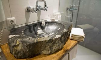 An elegant sink carved from a large piece of stone on a wooden table. In the background, modern fixtures and towels are visible.