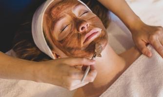 A woman is receiving a facial treatment at a spa. A therapist is applying a mask to her face.