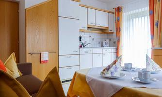 A modern kitchen with bright furniture and large windows. The dining table is set and offers space for a cozy meal.