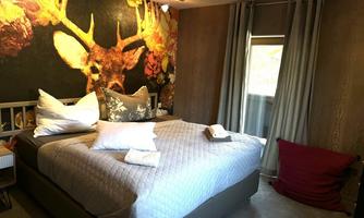 A cozy bedroom with a large bed and decorative pillows. The walls are adorned with a striking mural of a deer and colorful flowers.