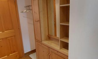 A spacious wooden wardrobe with open shelves. The floor is made of light wood and the walls are simple and bright.
