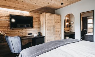 A cozy bedroom with wooden paneling and a large window. In the room, there is a television, a chair, and a desk.