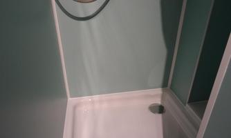A modern shower booth with a white shower area and blue walls. The shower has a flexible showerhead and a simple, clean design.