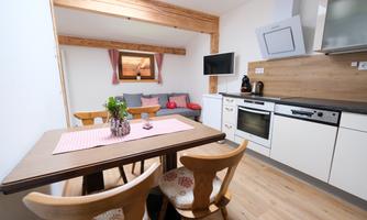 A modern kitchen with wooden elements and a dining table. The room is designed to be bright and friendly, with a cozy seating area.