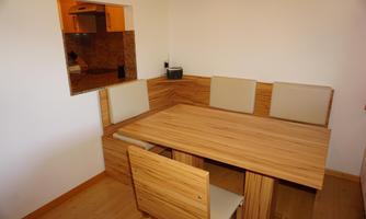 A cozy dining area with a wooden table and padded benches. The walls are bright, and the space feels inviting.