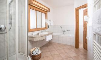 A modern bathroom with a shower, a bathtub, and a large window. The room is bright and inviting, with a basket full of toiletries.