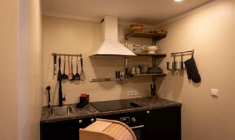 A modern kitchen with dark furniture and a functional setup. Kitchen utensils and dishes are hanging on the wall.