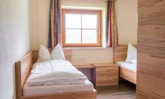 A cozy bedroom with two wooden single beds. The room has a window with curtains and light wooden flooring.